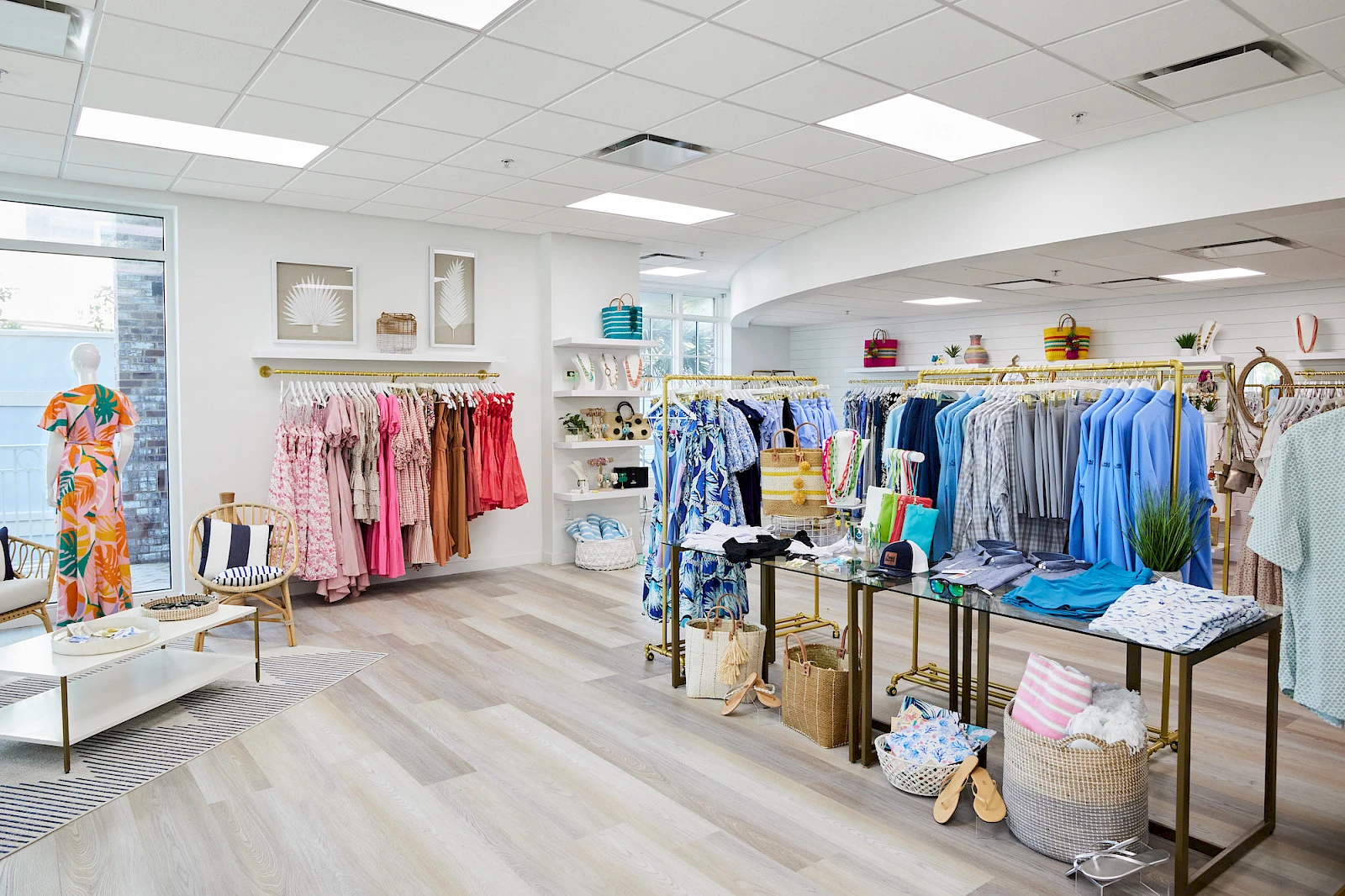 A bright boutique with racks of colorful clothing, shelves of accessories, a seating area, and light wooden floors, neatly arranged for shoppers.