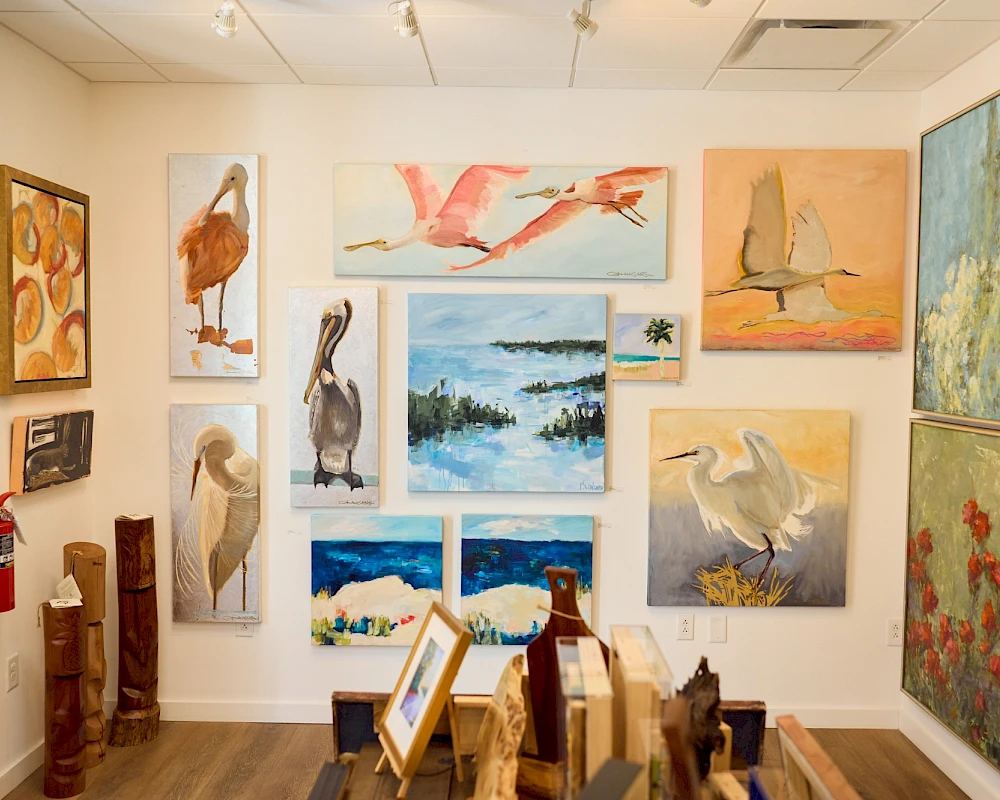 A bright gallery wall filled with animal and nature paintings, mostly birds, flamingos, pelicans, and seascapes, plus framed canvases and sculptures.