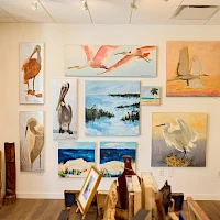 A bright gallery wall filled with animal and nature paintings, mostly birds, flamingos, pelicans, and seascapes, plus framed canvases and sculptures.