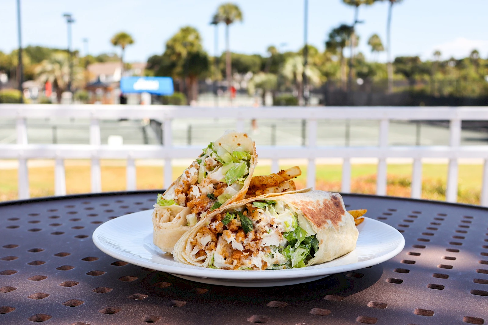 A plate of chopped falafel wrap with greens on a white plate, outdoors on a perforated table.