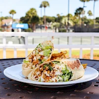 A plate of chopped falafel wrap with greens on a white plate, outdoors on a perforated table.