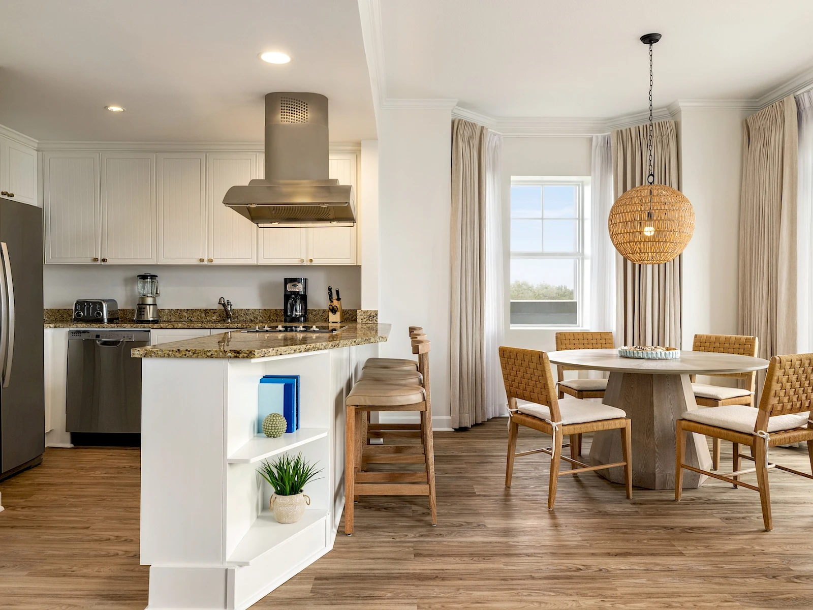 A modern open-plan kitchen and dining area with white cabinets, stainless appliances, a center island, and a cozy round table by windows.