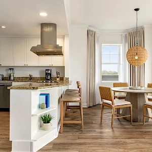 A modern open-plan kitchen and dining area with white cabinets, stainless appliances, a center island, and a cozy round table by windows.