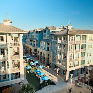 Cozy beachfront condo complex with pastel blue buildings, a central courtyard, and a row of blue umbrellas over outdoor tables.