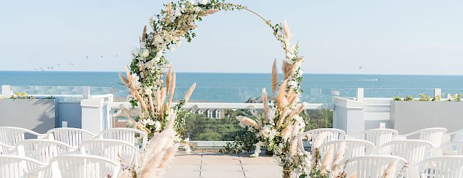 An outdoor wedding setup with white chairs, floral arrangements, and a decorative arch, overlooking a scenic ocean view.
