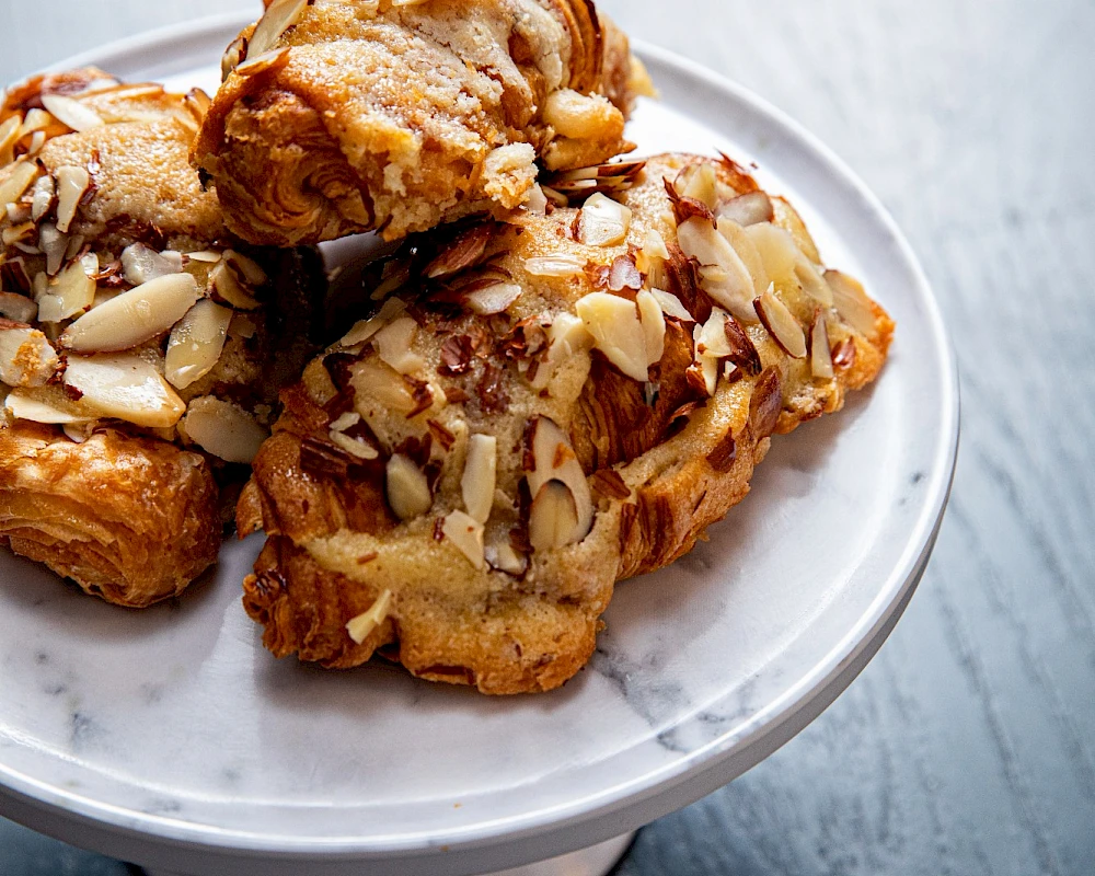 Delicious almond-topped pastries stacked on a small white pedestal, golden-brown and crunchy, perfect for a sweet tea time treat.