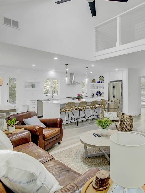 A modern, open-concept living room and kitchen with leather seating, wicker chairs, and a fireplace under a wall-mounted TV.