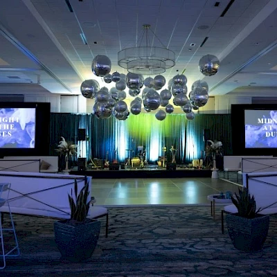 A conference or event stage with blue lighting, screens reading “MISSING DUNES,” podiums, and decorative orbs overhead in a formal venue. Yes.