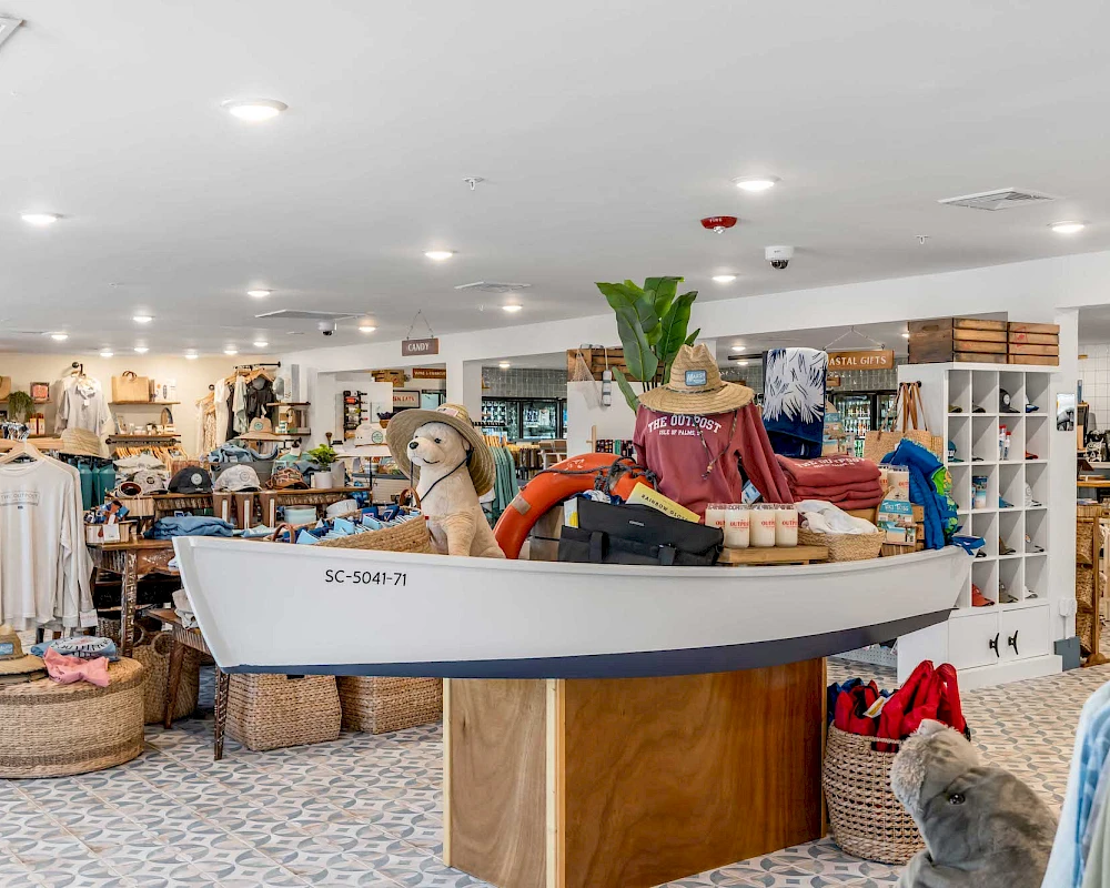 A white sailboat decor in a bright store, surrounded by clothing and baskets; shoppers’ shelves line the background, island display in the center.
