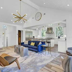 A bright, modern open-plan living area with a blue sofa, gold star chandelier, and a sleek kitchen; airy, stylish, and airy.