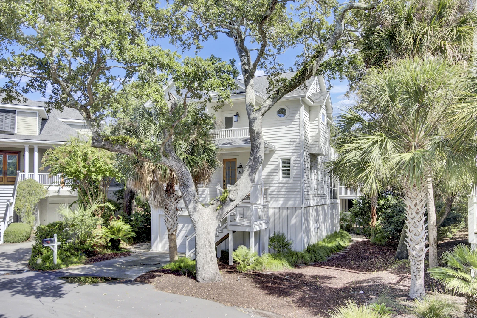 A light gray multi-story townhouse with white trim, surrounded by palm trees and landscaping; a driveway on the left.