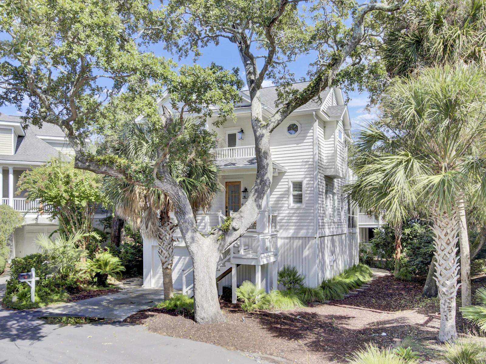 A light gray, two-story townhouse with white trim, front steps, surrounding trees, shrubs, and a small patch of mulch in the yard.
