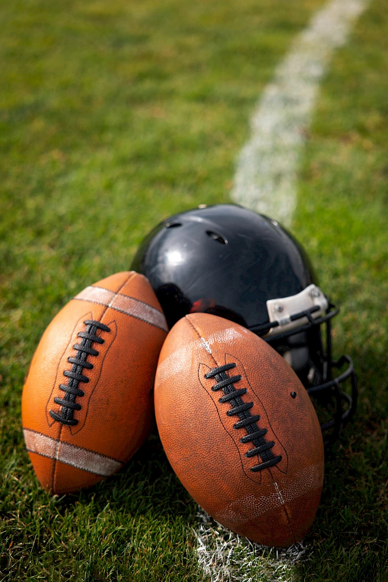 A football (American) and a black helmet resting on grass near the sideline line, bundled together at the edge of the field.